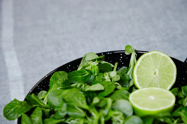 Watercress salad wit half split lime in wok black bowl close up — Stock Photo, Image