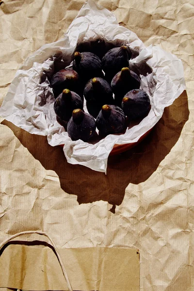 Figues on white craft paper in ceramic bowl on brown crafted paper — Stock Photo, Image