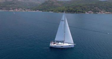 Sakin Mavi Deniz 'de süzülen yelkenli, Arka planda sahil tepeleri, güvertede dinlenen yolcular, suda parlayan güneş ışığı, hava aracı yakalama ve uyanma