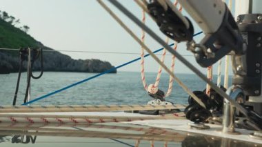 Yakından Çekilen Makara İpleri Ön Mürettebat Üyesi Foresail Donanımı, Mavi Deniz ve Rocky Sahil Hattı Arkaplanda, Pirinç Takımları, Gergin Çizgiler, Denizcilik Çalışmaları