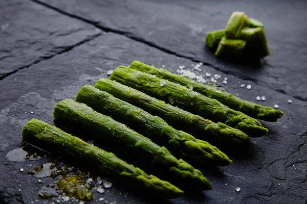 Whole and sliced asparagus with sea salt on black stone plate — Stock Photo, Image