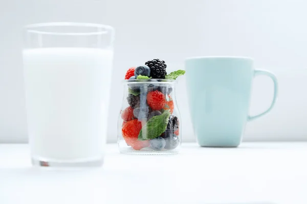Parallax Berries in transparent jar between glass of milk and blue cup — Stock Photo, Image