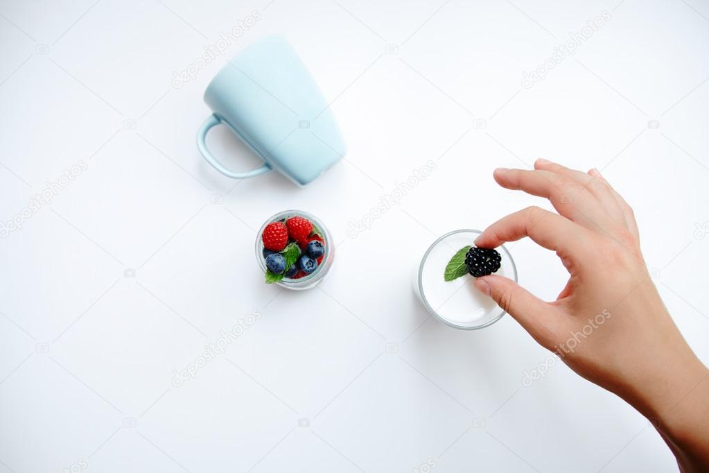 Hand puts blackberry in glass of milk, berries in transparent jar
