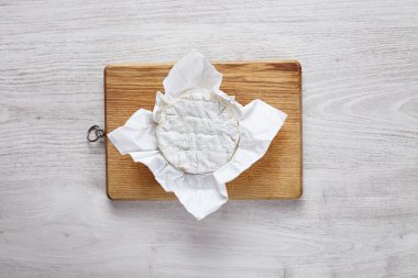 Camembert covered in white craft paper on wooden board isolated