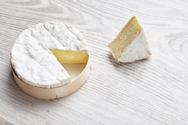 Camembert con trozo de ella, aislado en la mesa de la granja cepillado blanco — Foto de Stock