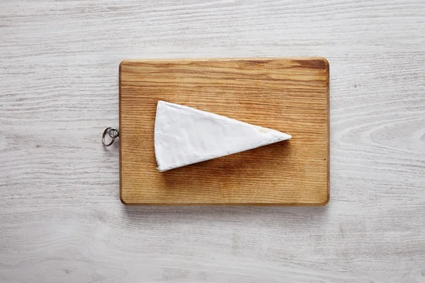 Całe miękkie Brie izolowane na desce do siekania na białym drewnianym stole — Zdjęcie stockowe