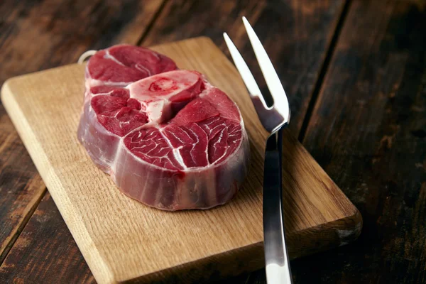Fresh meat steak with bone on wooden plate with big fork — Stock Photo, Image