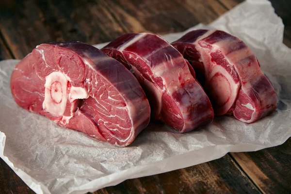 Three fresh meat steaks with bone white craft paper wooden table — Stock Photo, Image