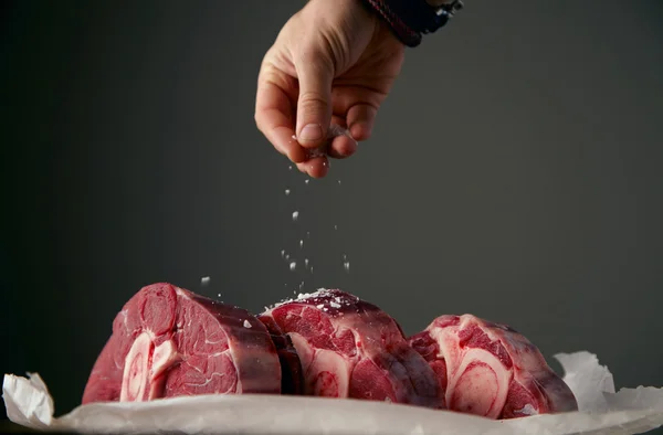 Hand is satling three fresh meat steaks with bone — Stock Photo, Image