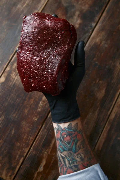 Tattooed right hand in black glove holds whale meat steak — Stock Photo, Image