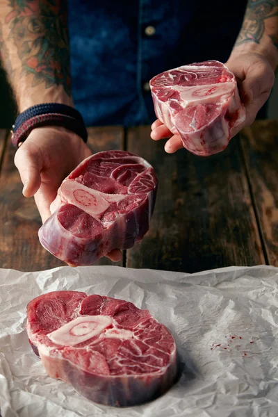 Deux steaks dans des mains tatouées et d'autres sur du papier artisanal — Photo