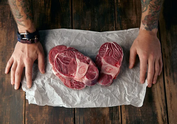 Vue du dessus de deux mains tatouées et trois steaks sur la table — Photo