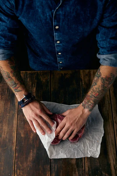 Tattooed hands pack steaks in white craft paper — Stock Photo, Image