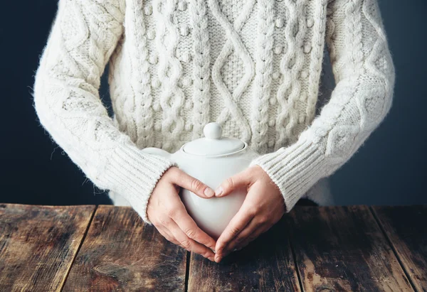 Mujer en suéter caliente toma las manos en la tetera blanca grande en forma de corazón —  Fotos de Stock
