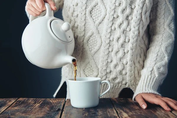在温暖的毛衣女人倒茶从茶壶到杯子里 — 图库照片