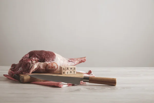 Pierna de cordero de carne cruda con letras sobre mesa blanca con cuchillo —  Fotos de Stock