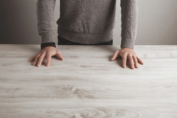 Man in grey sweater holds hands on table — 图库照片