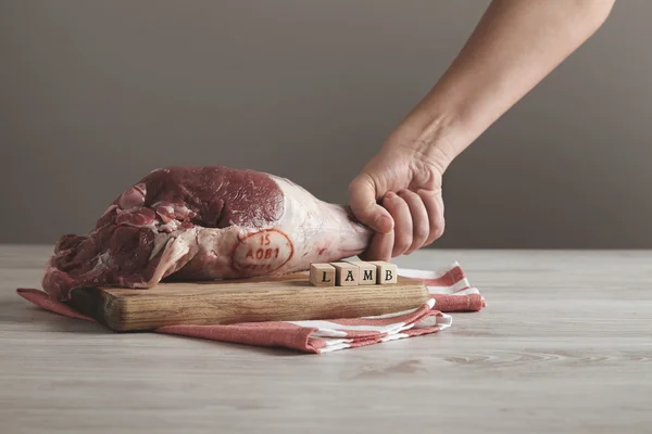 Mão detém carne crua perna de cordeiro na mesa — Fotografia de Stock