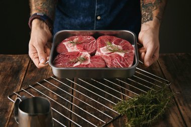 tattooed hands offers steaks in pan for camera