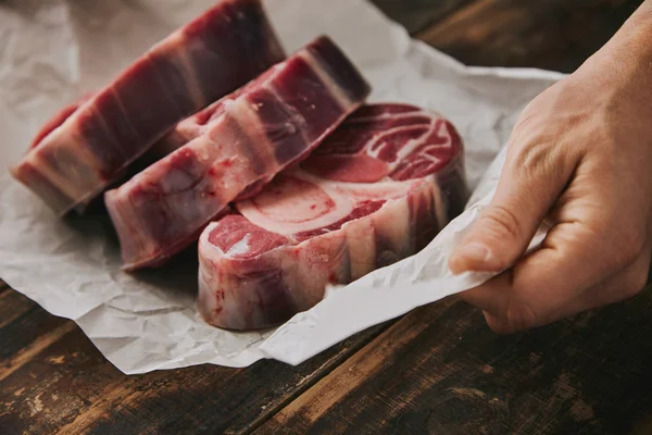 Mão de close-up segura papel branco três bifes crus — Fotografia de Stock