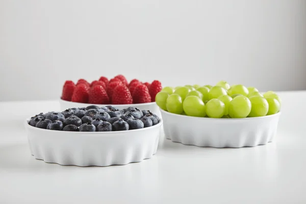 Heap of ripe raspberries blueberries grapes in ceramic bowls — 스톡 사진