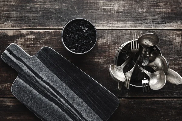 Mesa de pedra, sal preto, utensílios de cozinha na mesa — Fotografia de Stock