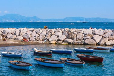Napoli, İtalya - 27 Mayıs Akdeniz kıyısında yaz günü. Mappatella Plajı 'ndaki dalga kırıcıda aşk koltukları olan çiftler. Koyda demirli tekneler var. 27 Mayıs 2012. Napoli, Campania, İtalya.