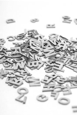 İnce kontraplaktan kesilmiş küçük ahşap harfler lazer kesiciyle beyaz arka planda rastgele istiflenmiş. B & W fotoğrafı.