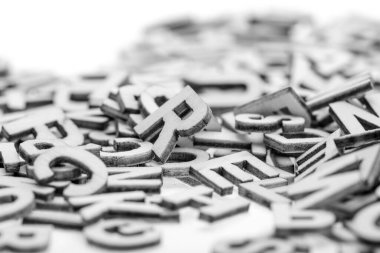 İnce kontraplaktan kesilmiş küçük ahşap harfler lazer kesiciyle beyaz arka planda rastgele istiflenmiş. B & W fotoğrafı.