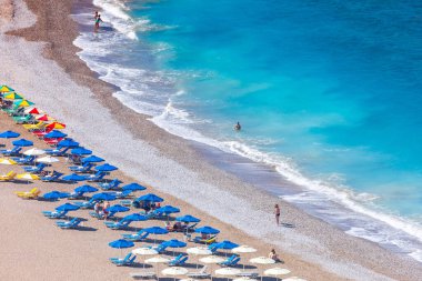 Boş bir sahil beldesinde renkli şemsiyeler ve güneşlikler - Ege ve Akdeniz 'deki Yunanistan adalarında tatil kavramı. Rodos 'ta Monte Smith' in altında Akti Kanari Plajı.