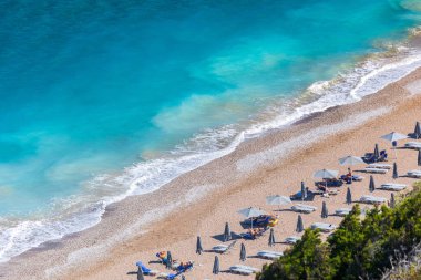 Boş bir sahil beldesinde renkli şemsiyeler ve güneşlikler - Ege ve Akdeniz 'deki Yunanistan adalarında tatil kavramı. Rodos 'ta Monte Smith' in altında Akti Kanari Plajı.