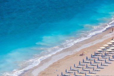 Boş bir sahil beldesinde renkli şemsiyeler ve güneşlikler - Ege ve Akdeniz 'deki Yunanistan adalarında tatil kavramı. Rodos 'ta Monte Smith' in altında Akti Kanari Plajı.