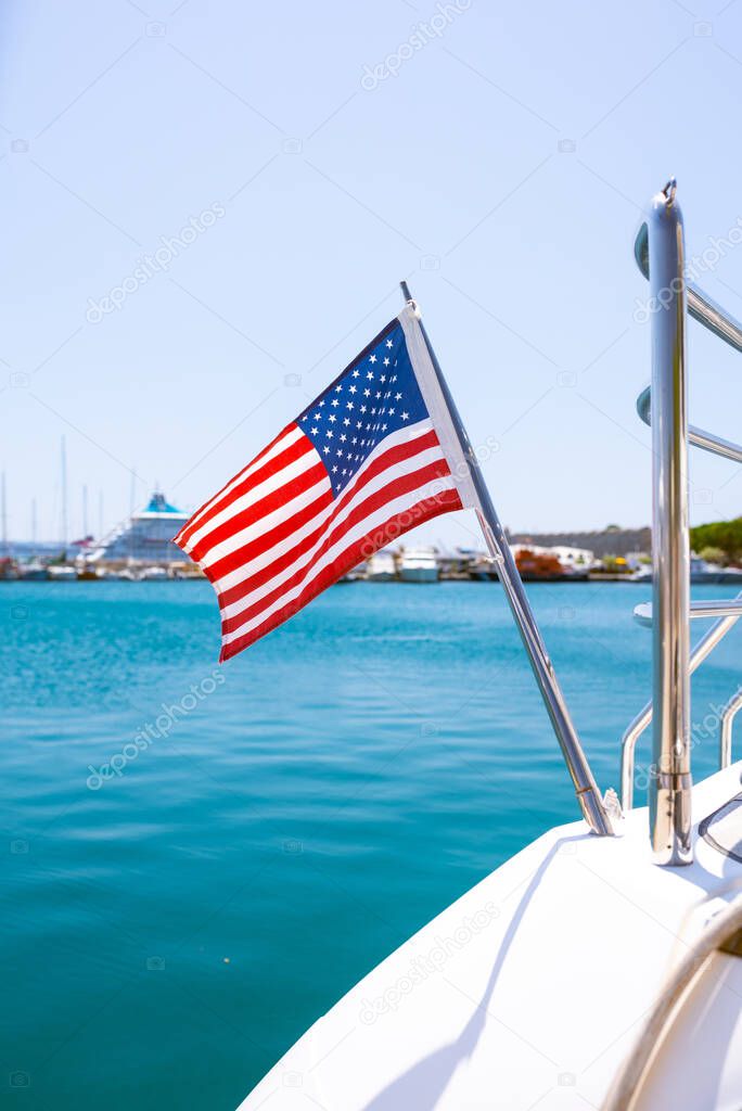 The flag of the United States flutters in the wind on a stainless steel flagpole at the stern of a motor yacht. Marina in the port city in beautiful summer sunny weather.