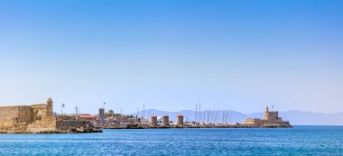 Rodos Heykeli 'nin yerine Mandraki limanı ve marinasının panoramik manzarası. Bağlanan yatlar ve gemiler. İskeledeki eski yel değirmenleri. Rodos, Dodecanese, Yunanistan 'da yaz tatili.