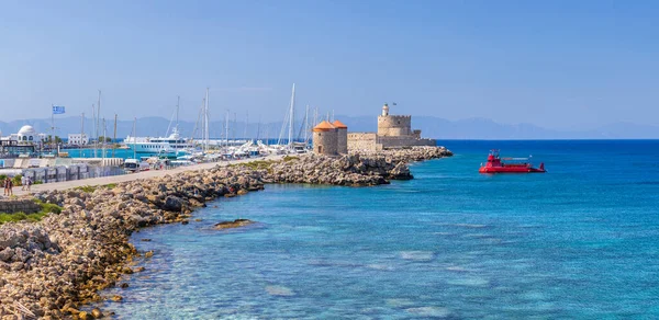 Rodos Heykeli 'nin yerine Mandraki limanı ve marinasının panoramik manzarası. Bağlanan yatlar ve gemiler. İskeledeki eski yel değirmenleri. Rodos, Dodecanese, Yunanistan 'da yaz tatili.