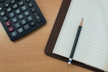hesap makinesi ve ahşap masa üstünde defter. Üstten Görünüm