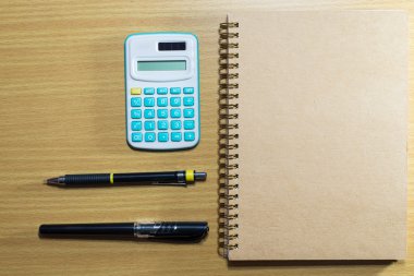 hesap makinesi, kalem, kurşun kalem ve defter ahşap masa üzerinde. Üstten Görünüm