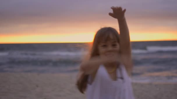 Urocza szczęśliwa dziewczynka w białej sukience na plaży o zachodzie słońca. — Wideo stockowe