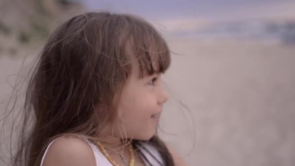 Rozkošná šťastná holčička v bílých šatech 4-5 let na bílé pláži při západu slunce. — Stock video
