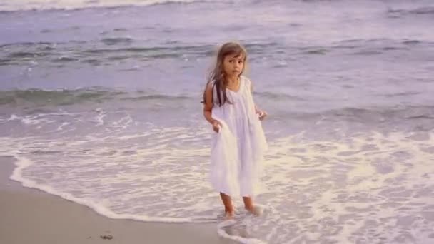 Rozkošná šťastná holčička v bílých šatech na bílé pláži při západu slunce. — Stock video
