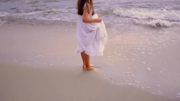 Adorável menina feliz em vestido branco nas ondas do mar ao pôr do sol. — Vídeo de Stock