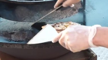 Eldivenli şef et pirzolası hazırlıyor. Mutfak spatulasıyla birlikte yuvarlak metal bir fırına koyuyor.