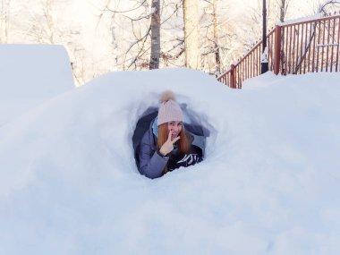Gülümseyen kız kar tünelinden dışarı bakan parmaklarıyla zafer işareti gösteriyor.