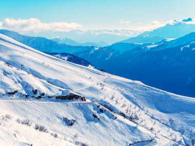 Arkaplanda karlı kayak yamaçları ve bulutlu mavi gökyüzü.