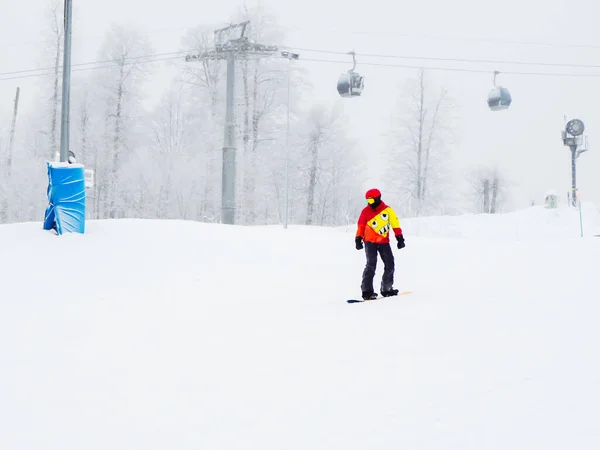 Russia, Sochi 21.01.2020. Snowboarder in giacca rossa e gialla cavalca oltre la funivia con tempo nebbioso — Foto Stock