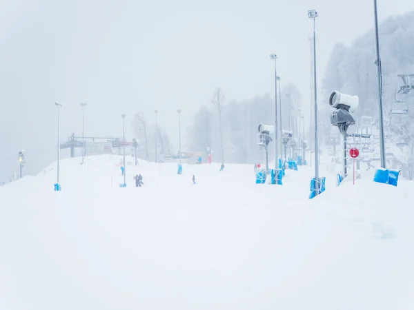 Canons à neige et projecteurs se tiennent le long d'une piste enneigée dans le brouillard lors d'une chute de neige — Photo