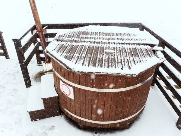 Wooden furaco hot tub stands on the terrace on a snowy winter day