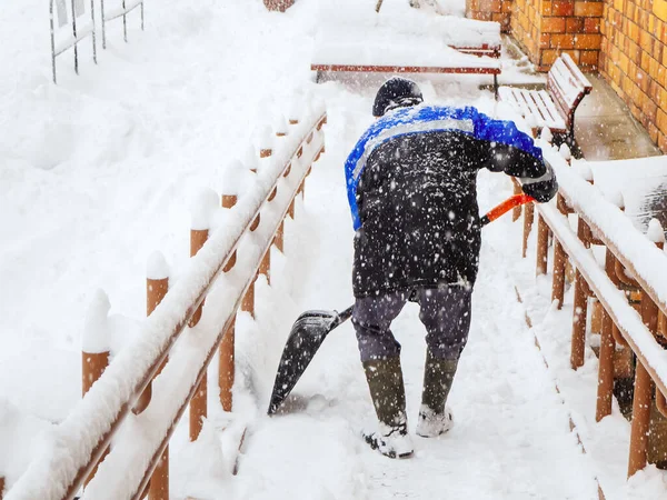 En arbetare rensar snö från verandan i ett hus under kraftigt snöfall — Stockfoto