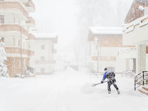 Bir işçi kar fırtınası sırasında sisli bir günde kulübelerin arasında kar temizler. — Stok fotoğraf