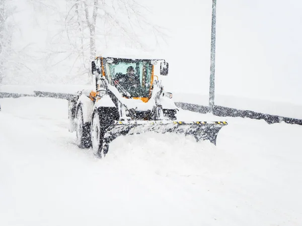 Traktor rensar snö från vägen under kraftigt snöfall och molnighet — Stockfoto